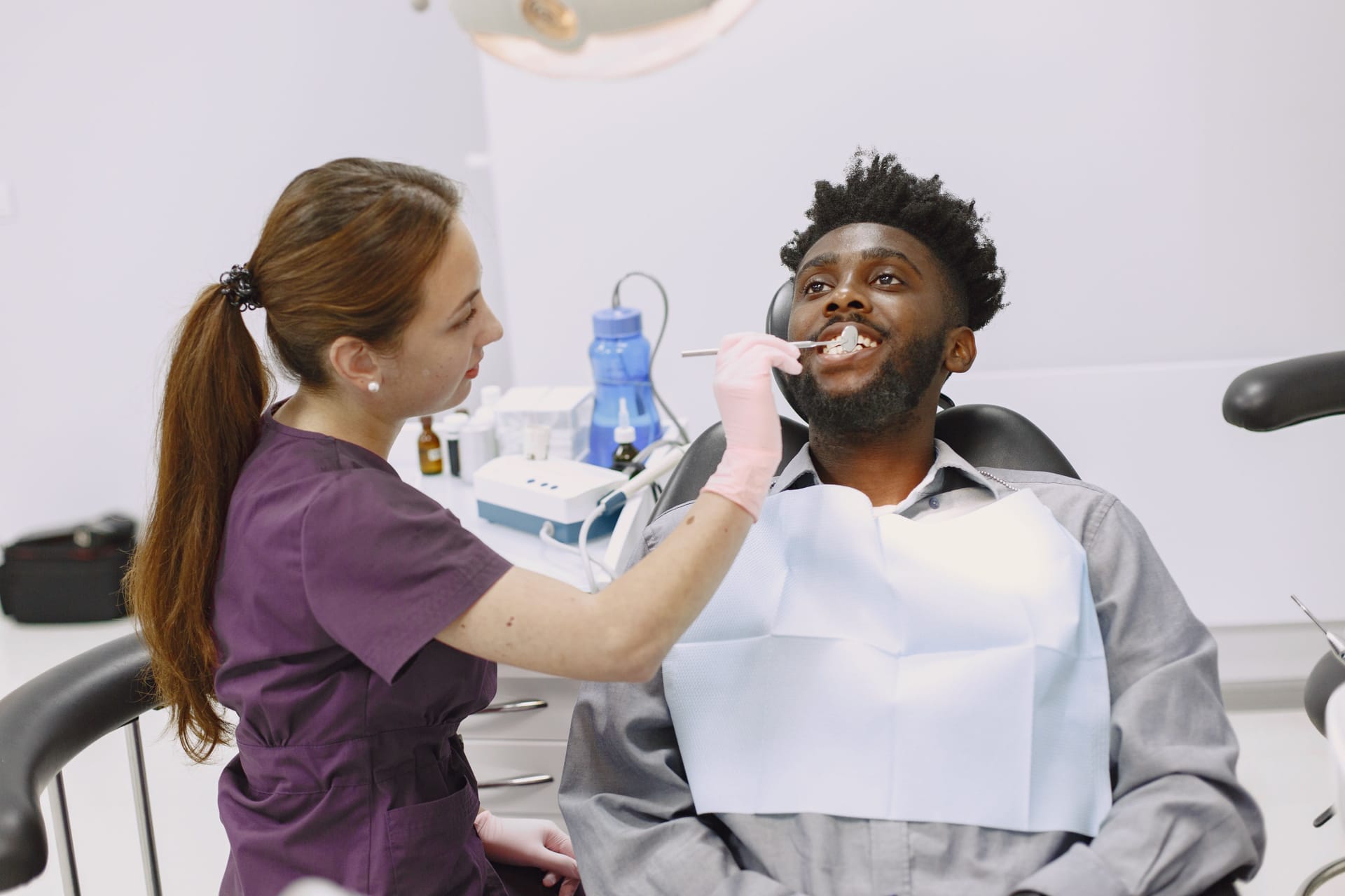Dentist in scrubs examining a smiling patient in a bright dental clinic